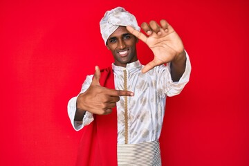 Canvas Print - Handsome indian man wearing tradition sherwani saree clothes smiling making frame with hands and fingers with happy face. creativity and photography concept.