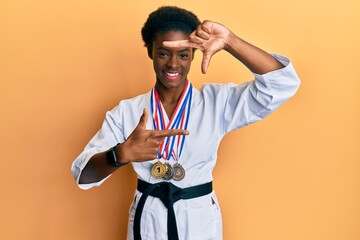 Poster - Young african american girl wearing karate kimono and black belt smiling making frame with hands and fingers with happy face. creativity and photography concept.