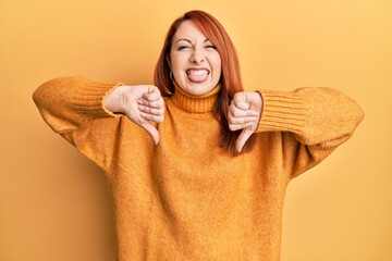 Poster - Beautiful redhead woman doing negative thumbs down gesture sticking tongue out happy with funny expression.