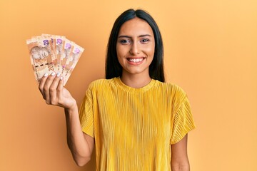 Poster - Young brunette woman holding south african 20 rand banknotes looking positive and happy standing and smiling with a confident smile showing teeth