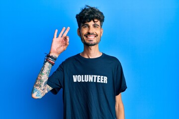 Young hispanic man wearing volunteer t shirt smiling positive doing ok sign with hand and fingers. successful expression.