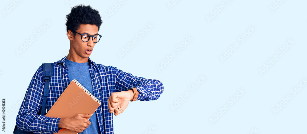 Young african american man wearing student backpack holding book looking at the watch time worried, afraid of getting late - obrazy, fototapety, plakaty 