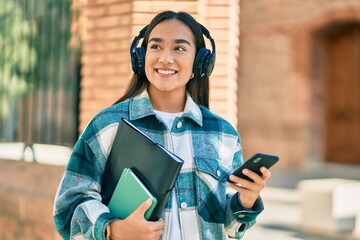 Sticker - Young latin student girl smiling happy using smartphone and headphones at the city.