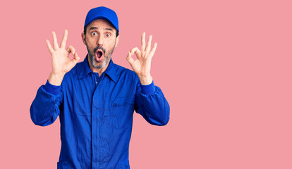 Canvas Print - Middle age handsome man wearing mechanic uniform looking surprised and shocked doing ok approval symbol with fingers. crazy expression