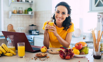 cute beautiful and happy young brunette woman in the kitchen at home is preparing fruit vegan salad 