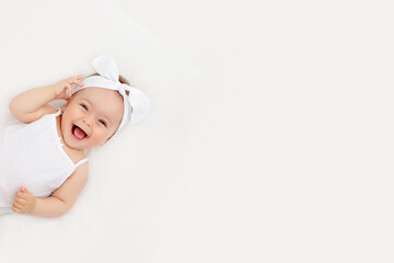 portrait of a smiling baby girl on a white bed at home, the concept of a happy, healthy baby, a plac