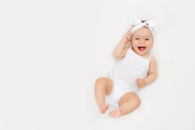 Smiling Newborn Baby On A White Bed At Home, The Concept Of A Happy, Healthy Baby, A Place For Text