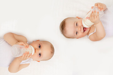 twin babies boy and girl with a bottle of milk on a white bed at home, baby food concept, place for 
