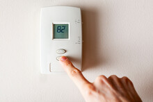 A Woman Is Pressing The Down Button Of A Wall Attached House Thermostat With Digital Display Showing The Temperature. A Concept Image For Electricity Bill, Heating, Cooling, Eco Friendly, Saving Etc.