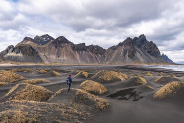 Vestrahorn mountain on Stokksnes cape in Iceland on a cloudy day with a man standing on one of the black sand dunes. One of the most famous travel locations in Iceland