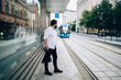 © BullRun - Stylish male looking at arriving tramway on empty city street