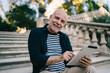 © BullRun - Half length portrait of happy senior traveller with modern touch pad gadget smiling at camera during free time in city, elderly male tourist 60s with digital tablet posing during vacations trip