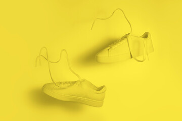 the concept of weightlessness and lightness. a pair of yellow sneakers flying in the air on a yellow background.