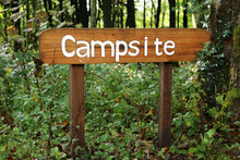 A Wooden Campsite Sign In The Middle Of A Forest
