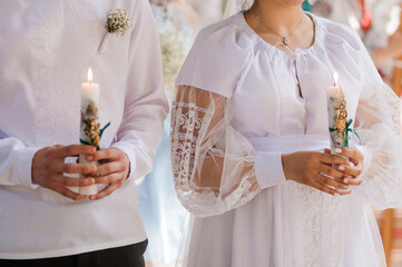 The bride and groom hold shining candles during the ceremony in the church. Hands of newlyweds with candles in the church. Church religious details. Traditions