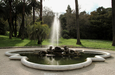 White marble fountain with water splash and bronze statues inside a city park.