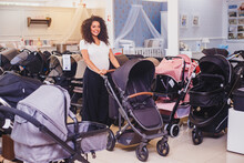 Afro Pregnant Woman Choosing Which Stroller She Wants To Buy, In A Maternity Goods Store For Babies, Enjoying Motherhood Thinking With Great Love About Her Future Child Who Is About To Be Born