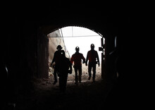 Silhouettes Of Men With Headlamps Walking Into Mine