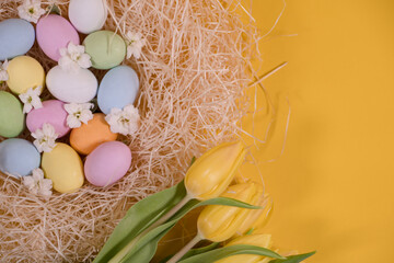 multicolored easter eggs on hay and near yellow tulips on yellow background