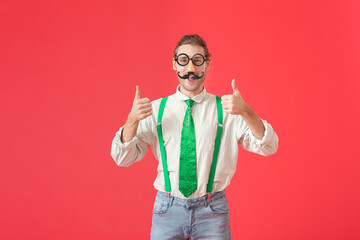 Poster - Young man in funny disguise showing thumb-up gesture on color background. April Fools Day celebration