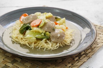 Wall Mural - A plate of I Fu Mie or Crispy Fried Noodle with thick savory sauce and meatball and vegetables in shiny and grainy white background. Selective focus