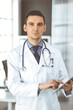© cameravit - Friendly male doctor using tablet computer in clinic near his working place. Perfect medical service in hospital. Medicine and healthcare concept