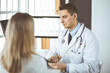 © cameravit - Friendly male doctor and patient woman discussing current health examination while sitting in clinic. Perfect medical service in hospital. Medicine and healthcare concept