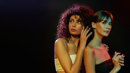 Wall Mural - Two attractive half naked young brunette women with professional art makeup posing together in neon light isolated over black background