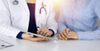 © rogerphoto - Unknown woman-doctor is showing to her patient a description of medication, while sitting together at the desk in the sunny cabinet in a clinic. Female physician is using a computer tablet and a