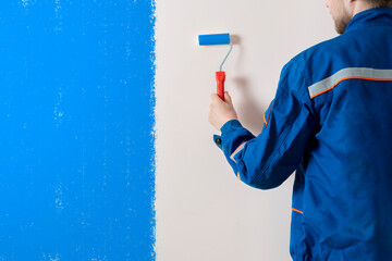 Wall Mural - worker painter painting the wall surface with a roller, man at work decorating a room