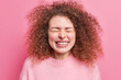 © wayhome.studio  - People and happiness concept. Glad curly haired young European woman smiles broadly feels very happy closes eyes squints at camera dressed in casual jumper isolated over pink studio background.