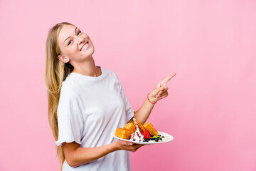 Wall Mural - Young russian woman eating a waffle isolated excited pointing with forefingers away.