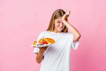 Wall Mural - Young russian woman eating a waffle isolated forgetting something, slapping forehead with palm and closing eyes.