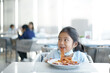 © kornnphoto - Asian child smile or kid girl wearing face mask under chin to enjoy eating delicious food by grilled bacon sausage on white dish with happy lunch or breakfast in morning at restaurant or food court