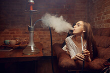 Young Woman Lying On Sofa And Smokes Hookah In Bar