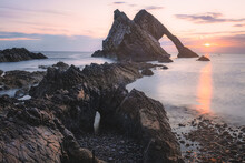 Beautiful Dramatic Sescape Scenery At Sunrise Or Sunset Of Bow Fiddle Rock Sea Arch On The Rocky Shore Of Portknockie On The Moray Firth In Scotland.