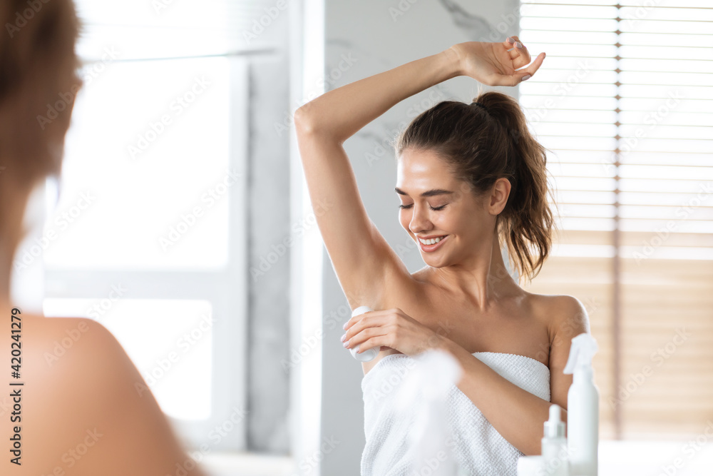 Woman Applying Antiperspirant On Armpits Preventing Sweating Standing In Bathroom - obrazy, fototapety, plakaty 