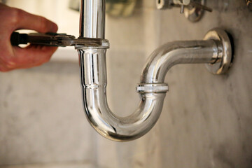 Plumber fixing sink pipe with adjustable wrench.