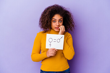 Young African American woman holding a gender equality placard isolated on purple background biting fingernails, nervous and very anxious.