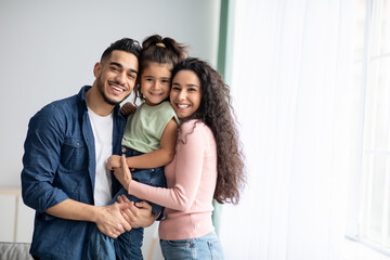 portraif of happy arabic parents posing with their little daughter at home
