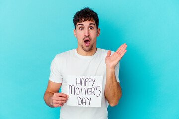 Wall Mural - Young caucasian man holding a happy mothers day placard isolated surprised and shocked.