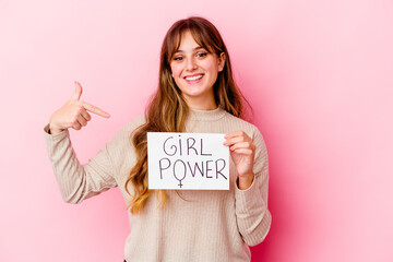 Wall Mural - Young caucasian woman holding a girl power placard isolated on pink background person pointing by hand to a shirt copy space, proud and confident