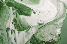 Acrylic Fluid Art. White Foamy Vortices On Green Background. Flow Of Colors On Canvas. Abstract Stone Background Or Texture