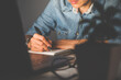 © Baramee - Close up of people hand writing something on notebook in office at night for business and finance.Work from home concept.