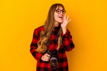 Wall Mural - Young photographer caucasian woman isolated on yellow background shouting and holding palm near opened mouth.