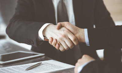 Unknown businessmen shaking hands above the glass desk in a modern office, close-up. Unknown business people at meeting. Teamwork, partnership and handshake concept