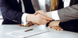 © Iryna - Unknown businessman shaking hands with his colleague or partner above the glass desk in modern office, close-up. Business people group at meeting
