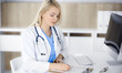 © Iryna - Woman-doctor at work while sitting at the desk in hospital or clinic. Blonde cheerful physician filling up medication history record form