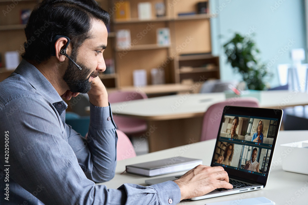 Indian business man wearing headset having virtual team meeting on video conference call, using laptop work from home office talking to diverse people group in remote teamwork online distance chat. - obrazy, fototapety, plakaty 