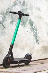 Electric scooter standing against bright wall background. E-scooter or kick scooter using with mobile app. Modern, ecological, eco-friendly urban transport. Summer in the city. Copy space, close up